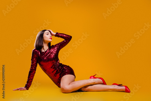 Bild auf Leinwand Glamorous woman in a red sequin dress and red high heels posing on an orange stu