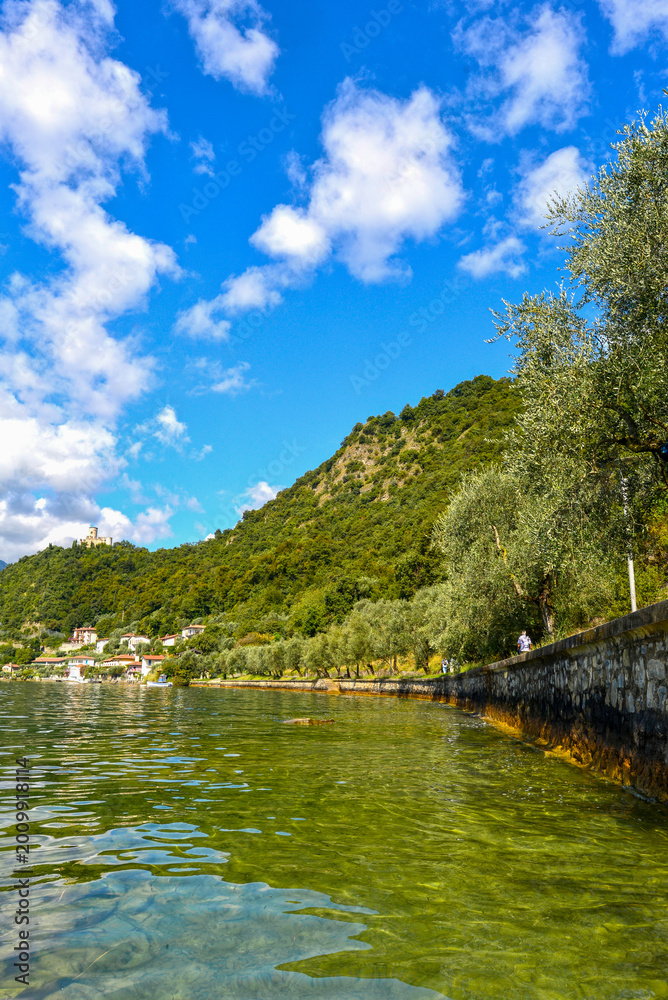 Fototapeta premium Blick über den Iseosee auf die Burg Rocca Martinengo und die umliegenden Berge, Italien
