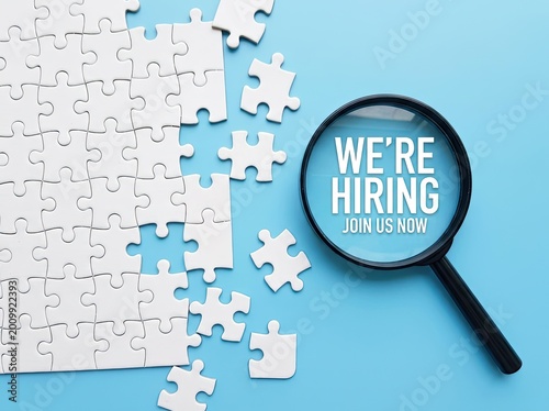 White puzzle pieces scattered next to a magnifying glass with the phrase 'we're hiring,' blue background, recruitment Concept.