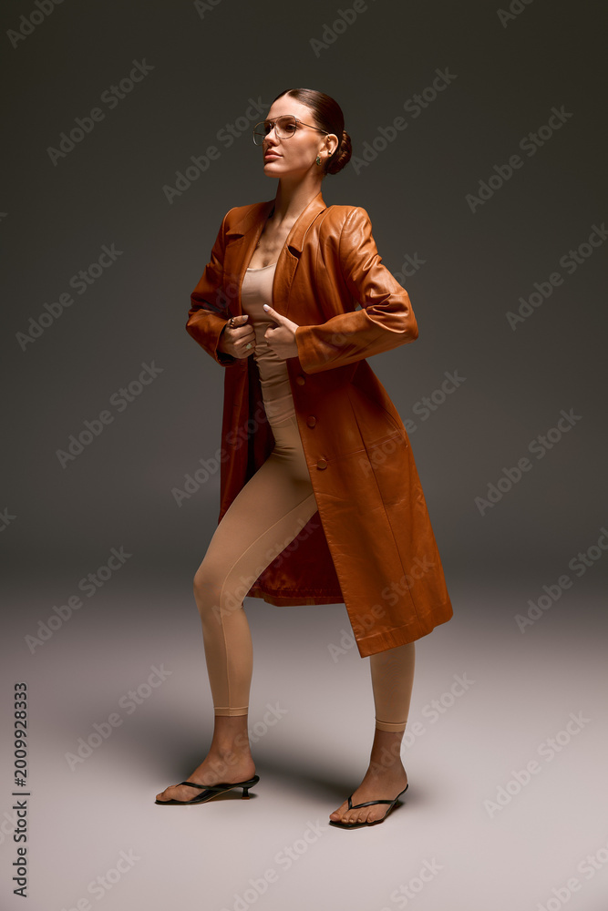 Fototapeta premium Stylish young woman in a leather coat showcasing modern fashion in a studio setting