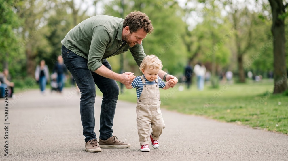 Obraz premium Father assisting toddler with first steps in park during spring 