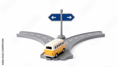 Toy traffic sign representing a choice of two paths styled as a miniature road decision scene with a central signpost a curved road segment leading left and right and a tiny toy bus positioned at the