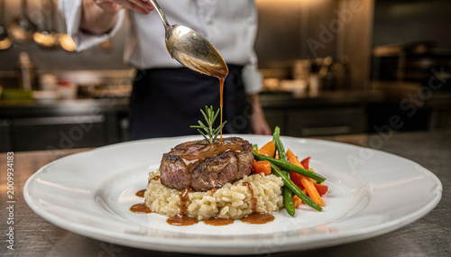Cuadro en lienzo Professional Chef Garnishes Gourmet Beef Dish with Sauce in Kitchen Setting