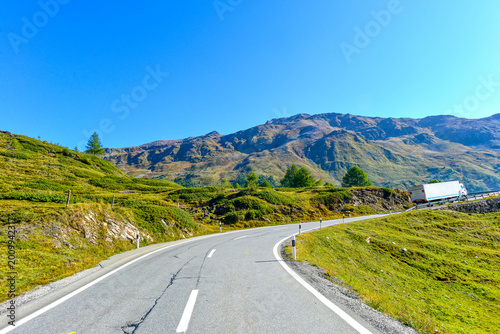 Foto Langgezogene Kurve der Berninapassstrasse mit Leitplanke vor markanten Alpengipf