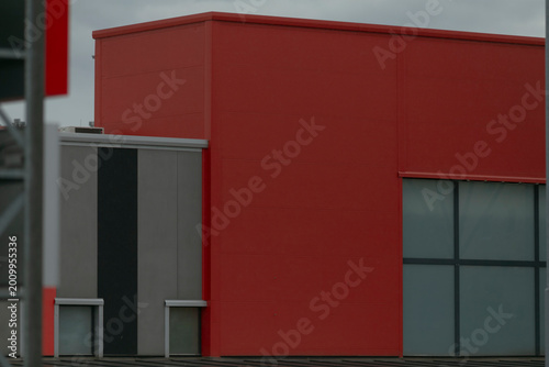 Bold red commercial building with large windows and gray accents, blocky volumes and crisp lines create dynamic urban presence modern facade panels and industrial scale suggest