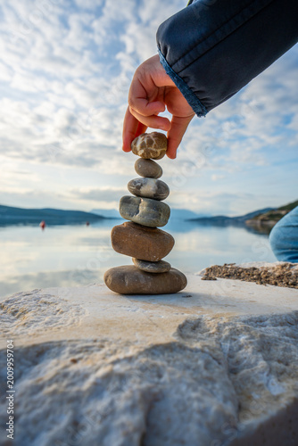 Child Balancing Stones With Left Hand by Calm Sea With Dramatic Cloudy Sky