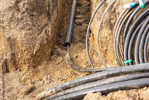 Bild auf Leinwand Thick walled plastic protective pipe and armored cables in excavation trench for