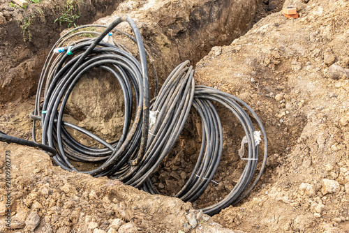 Coiled armored power cables in excavation trench for underground utility installation in clay soil construction site
