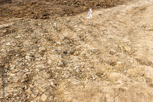 Fotografie Geodetic survey stake with red and white signal tape on prepared clay ground bas