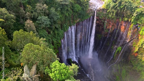 Aerial drone view of Tumpak Sewu waterfall in East Java, Indonesia. Spectacular curtain waterfall surrounded by dense tropical jungle and cliffs, showcasing powerful cascading water and natural beauty