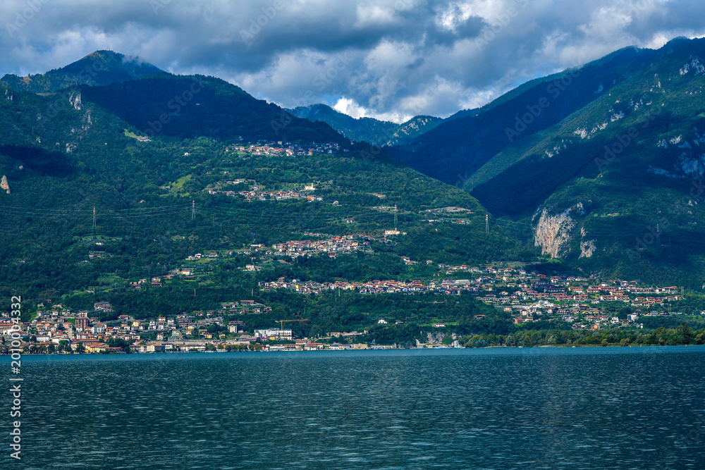 Fototapeta premium Blick über den Iseosee auf die gestaffelte Hangsiedlung von Castro vor den Bergamasker Alpen, Italien