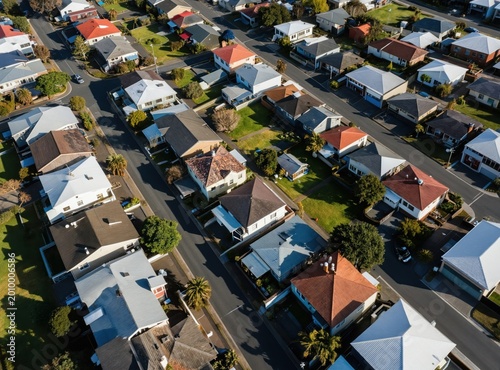 Aerial view of residential neighborhood rooftops in South Auckland, New Zealand. Suburban houses with varied roof styles line quiet streets, showing neat lawns and green spaces during daylight.