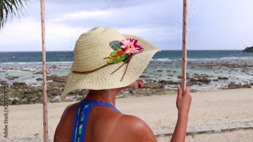 A woman seated on a coastal swing enjoys the coastal breeze on a tropical island.