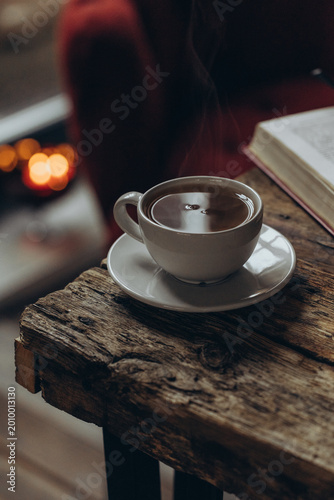 Home decor and comfort. A book, glasses, and a cup of tea on a wooden table. A sitting area in a cozy room. 