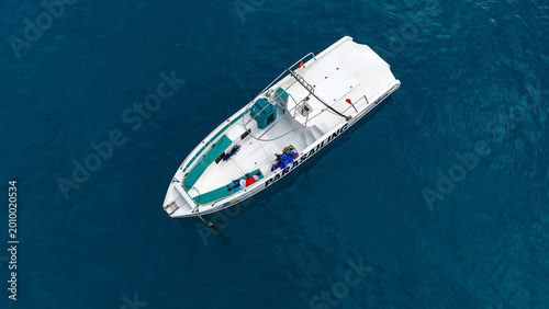 Incredible top down aerial capture of a pristine white luxury motor yacht with distinctive turquoise deck accents floating completely alone on the vibrant blue surface of the open sea