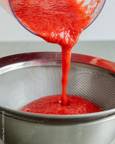 Принти на полотні Close-up of strawberry puree being strained through a fine-mesh sieve into a bow