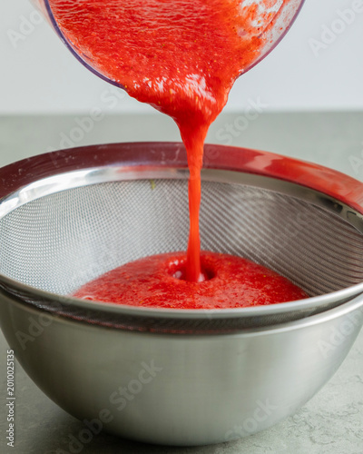 Fényképezés Close-up of strawberry puree being strained through a fine-mesh sieve into a bow