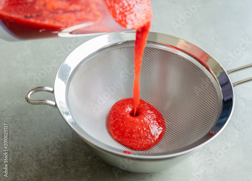 Schilderij op canvas Close-up of strawberry puree being strained through a fine-mesh sieve into a bow