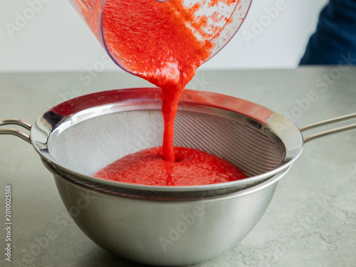 Tableau sur toile Close-up of strawberry puree being strained through a fine-mesh sieve into a bow