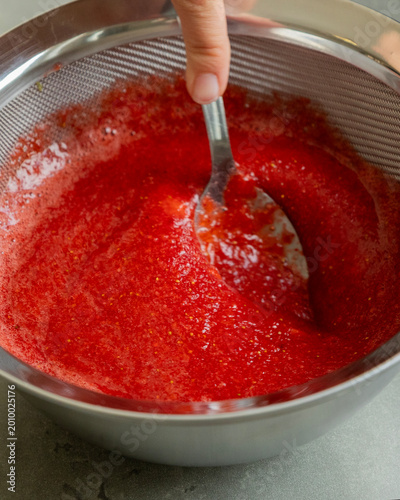 Fotografia Close-up of strawberry puree being strained through a fine-mesh sieve into a bow