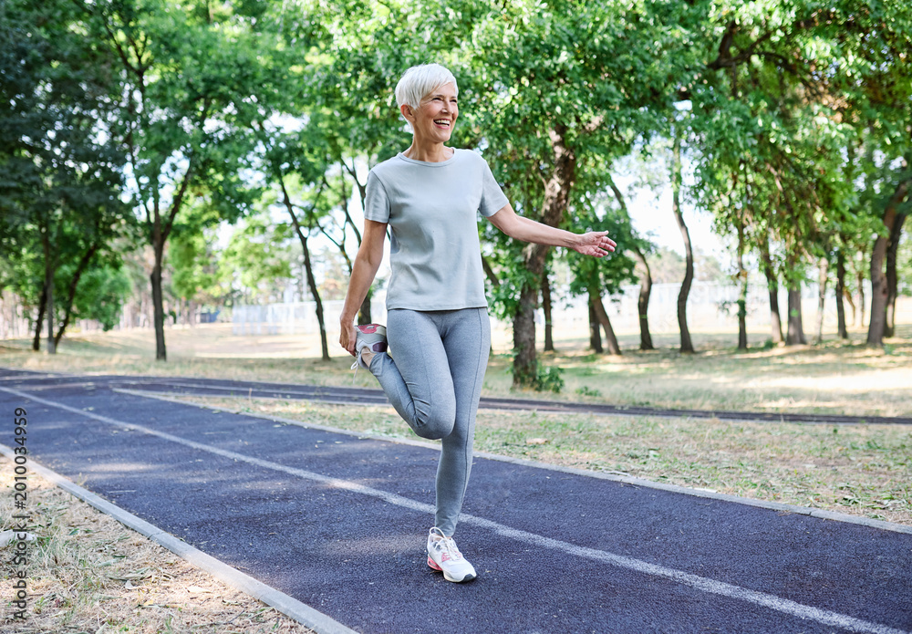 Naklejka premium Portrait of a senior mature woman exercising, stretching, warming up, running and jogging outdoors in the park