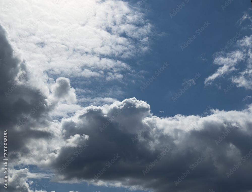 Naklejka premium Dramatic clouds fill a blue sky. Bright and dark cloud layers create a strong weather scene. Natural background for design and copy space..