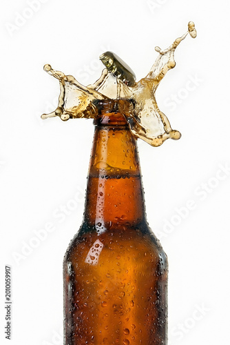 Brown glass beer bottle with cap flying off and splashing liquid. Refreshing alcoholic drink with carbonated beverage explosion. Cold beverage, pub culture and party celebration concept.