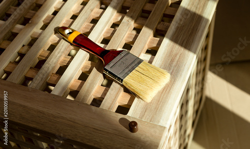 Paintbrush resting on an acacia wood lattice box. Warm sunlight and surface finishing detail on a wooden storage piece. DIY furniture care and refinishing concept..