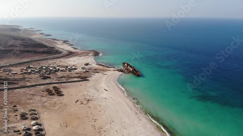 Panoramic aerial video of Socotra Island's coastline featuring an abandoned shipwreck on a turquoise beach, ideal for travel, historical, and adventure themes