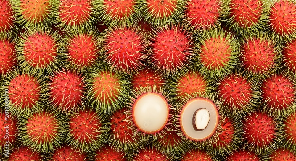 Fototapeta premium vibrant red spiky lychee fruits with peeled white flesh on green textured background for summer tropical freshness
