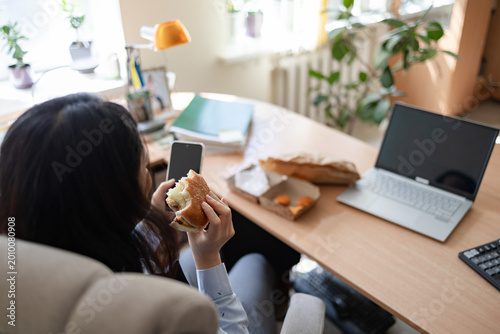 Fotografija Asian young businesswoman eating fast food while working in office