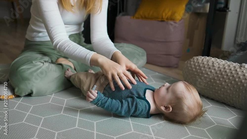 Young woman exercising with infant child on a play mat, healthy lifestyle concept. Smiling mom playing and bonding with little boy at home.
