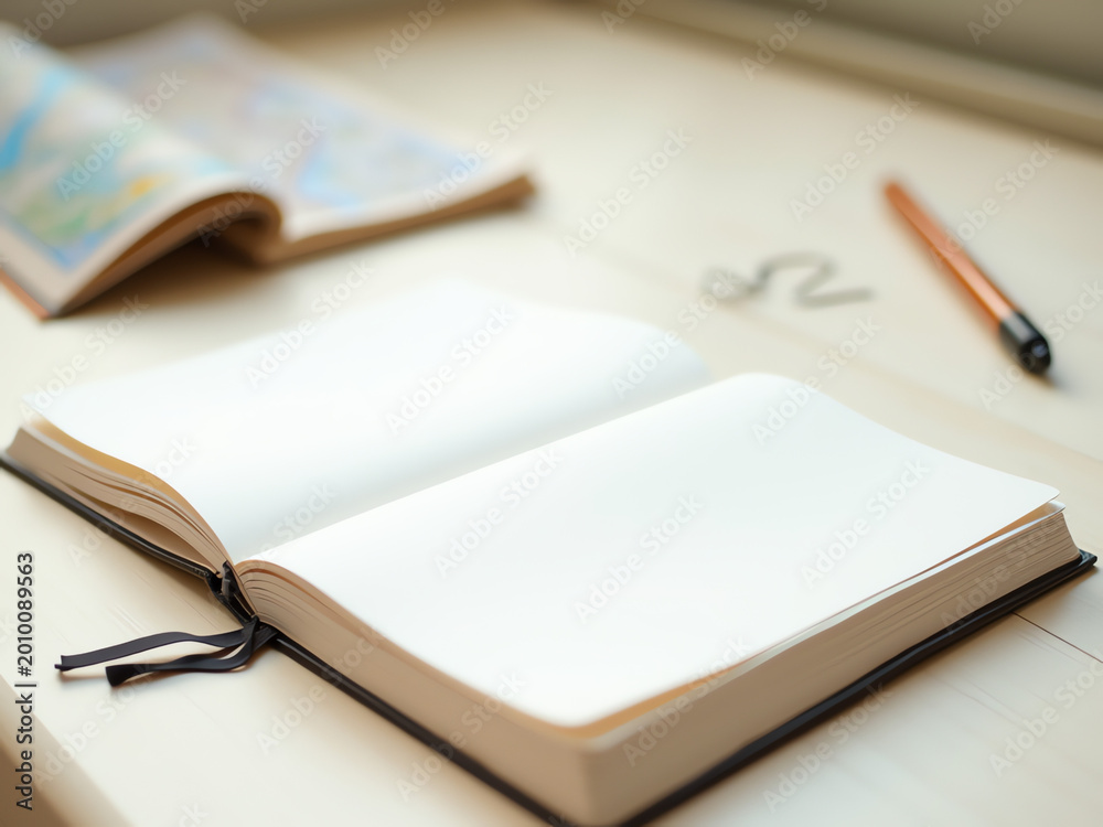Fototapeta premium Blank notebook and pen on wooden desk with open map in background 