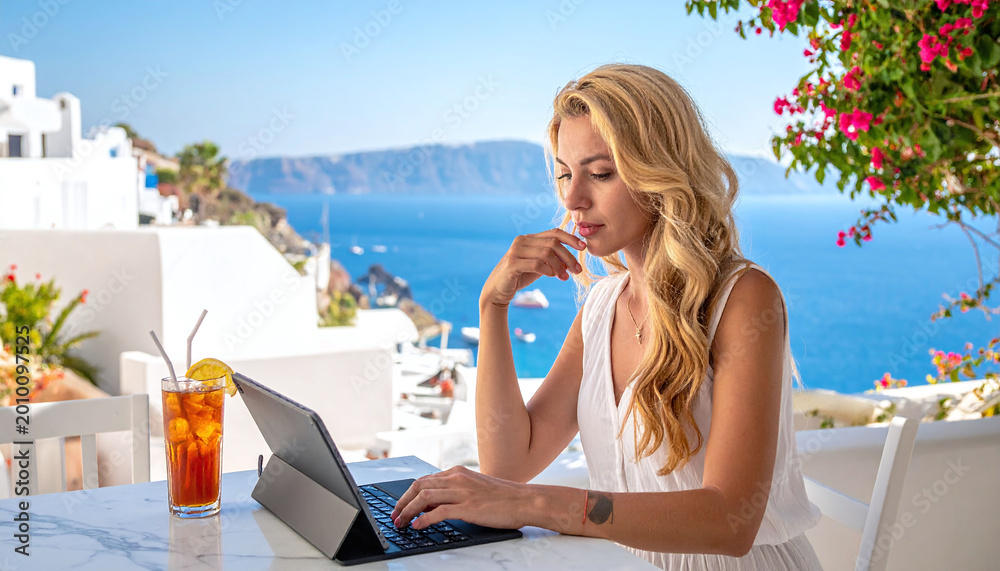 Naklejka premium Focused blonde woman working remotely on a tablet in Santorini, Greece. Scenic sea views and white architecture create a luxury lifestyle theme for digital nomads and business.