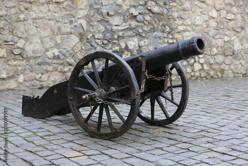 Antique black cannon with wooden wheels on cobblestone ground