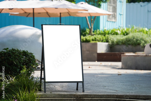 Blank white outdoor advertising stand sandwich board mock up template. Clear street signage board placed by an outdoor dinning area of a restaurant.