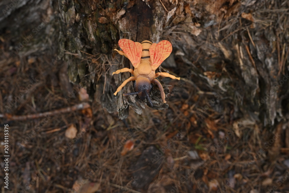 Fototapeta premium Toy insect resembling a bee sitting on a tree stump, illustrating artificial life and habitat concept