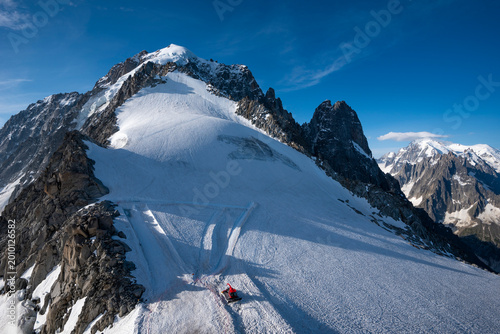 Fotografía Snowcat grooming fresh snow on a ski slope during early morning, with rugged peaks of Aiguille des Grands Montets and Aiguille Verte (4