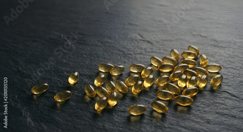 Close-up of scattered golden capsules on dark textured surface emphasizing details and reflective qualities