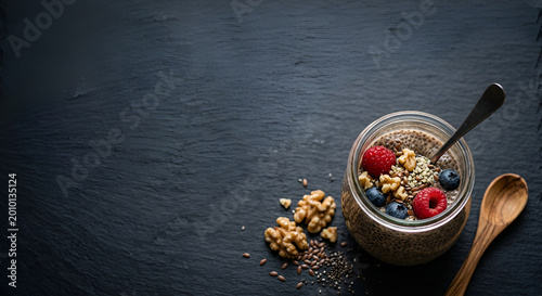 delicious chia pudding with fresh berries and nuts served in a glass jar on dark wooden surface