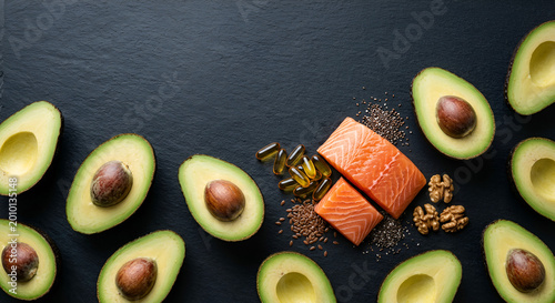 Fresh avocado halves and raw salmon fillets with walnuts and supplements on a dark surface