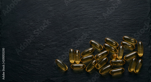 Close-up of scattered vitamin capsules reflecting light on a dark textured surface emphasizing supplement intake and nutritional