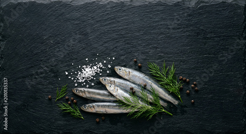 Fresh sardines with herbs and spices arranged on dark textured surface for culinary presentation