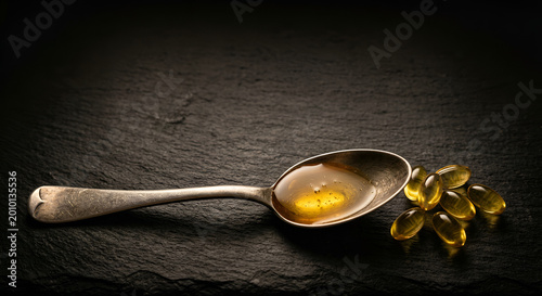 Golden fish oil capsules scattered on dark textured surface with a vintage spoon for supplements healthcare and wellness dietary