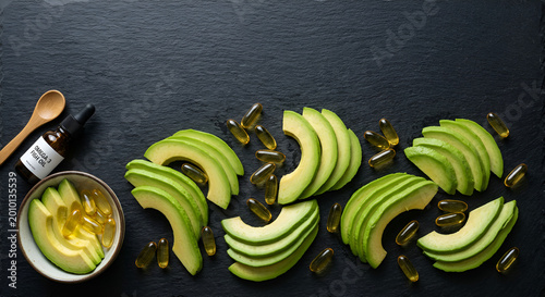 Healthy avocado slices with dietary supplements and omega-3 capsules on a dark textured surface for nutritious diet options