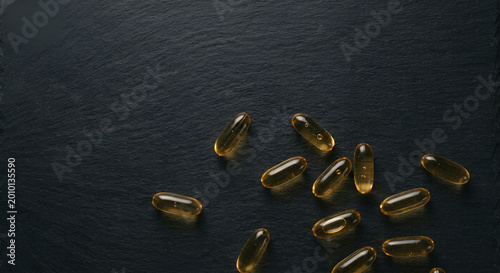 glistening softgel capsules arranged on dark textured surface for supplement storage or health boost concepts with minimalistic