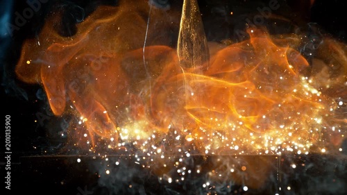 Close-up of blacksmith forging glowing hot iron on anvil with flying sparks. Super slow motion filmed on high-speed cinema camera at 1000 fps