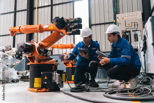 Industrial robot arm auto assembly in factory with engineer teamwork control panel safety helmet inspection training focus