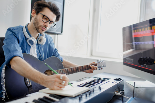 Fotografie Male music arranger composing song on midi piano and audio equipment in digital recording studio