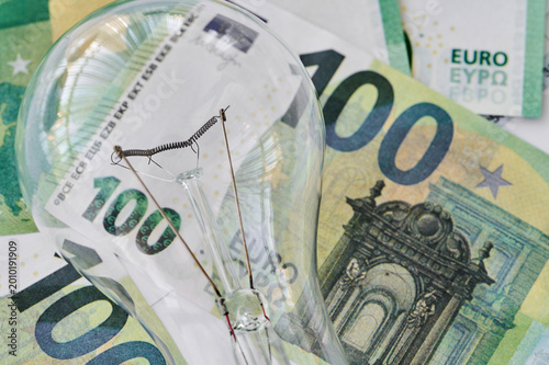 A light bulb sits on a pile of euro banknotes, representing the relationship between energy and money in daily life.